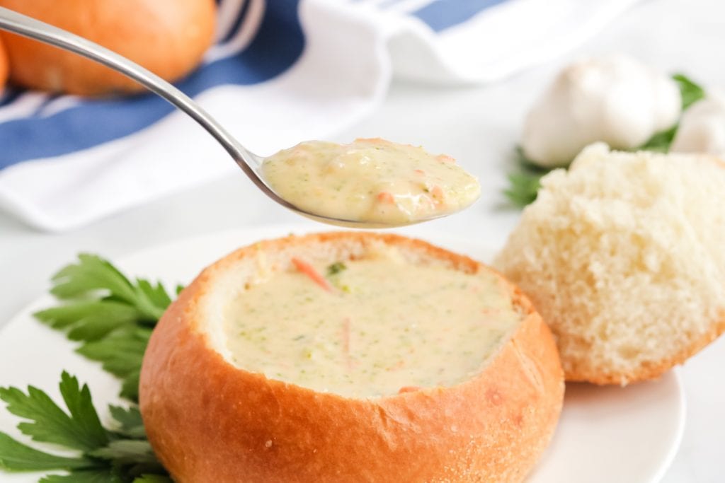 Spoonful of Copycat Panera Broccoli Cheddar Soup with a bread bowl in background