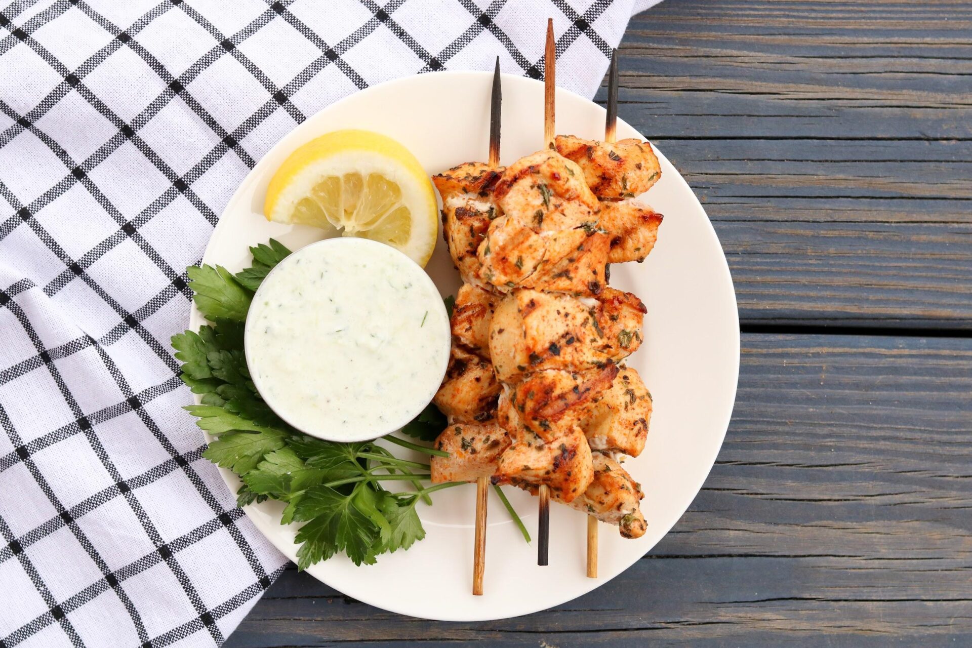 Greek Chicken Kebobs on white plate skewered with blue check napkin