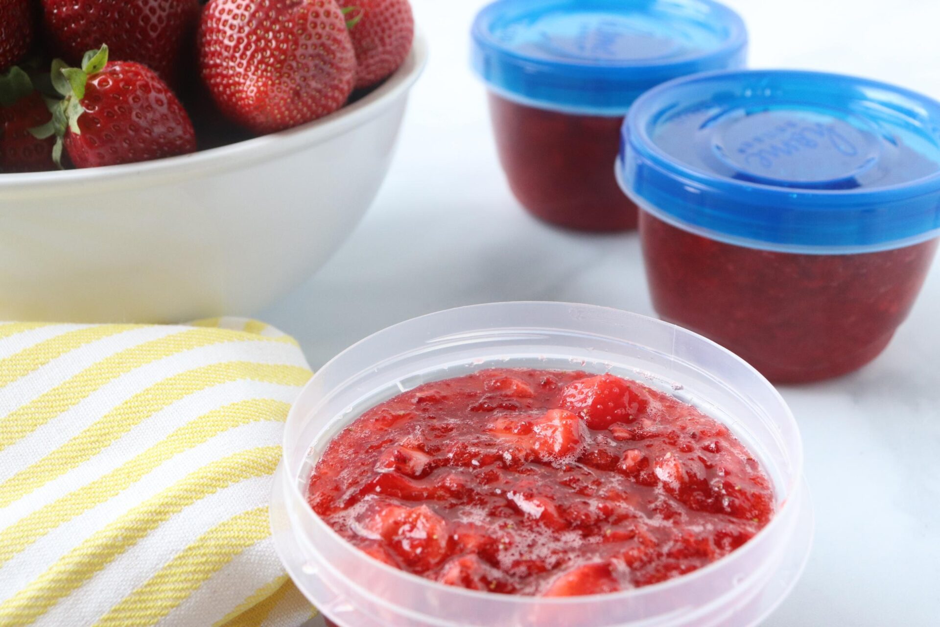 strawberry freezer jam in a plastic storage container with yellow linen. 