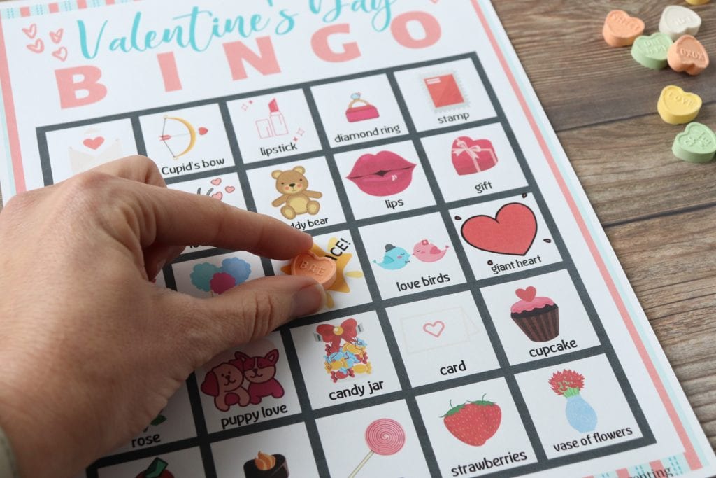 Valentine's Day Bingo sheet with heart candies a hand putting a heart candy on the free space.