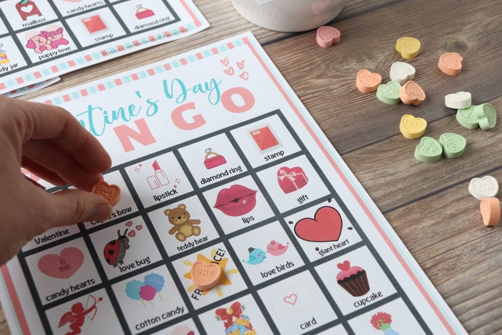 Valentine's Day Bingo sheet with heart candies. One heart candy on the free space and a hand putting a heart candy on the Cupid's bow space.