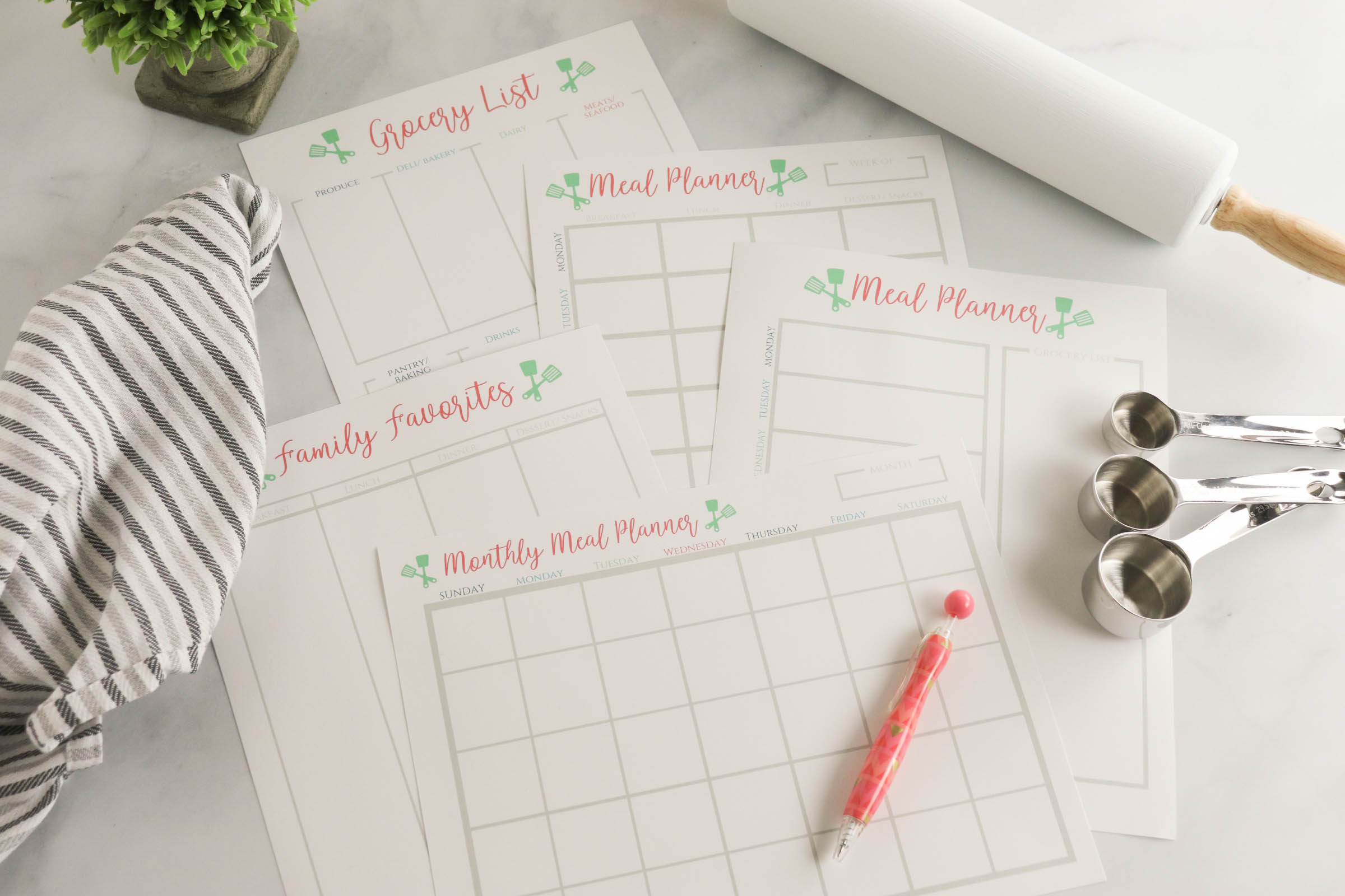 Meal planner printables with measuring spoons, pen, dishcloth and rolling pin.