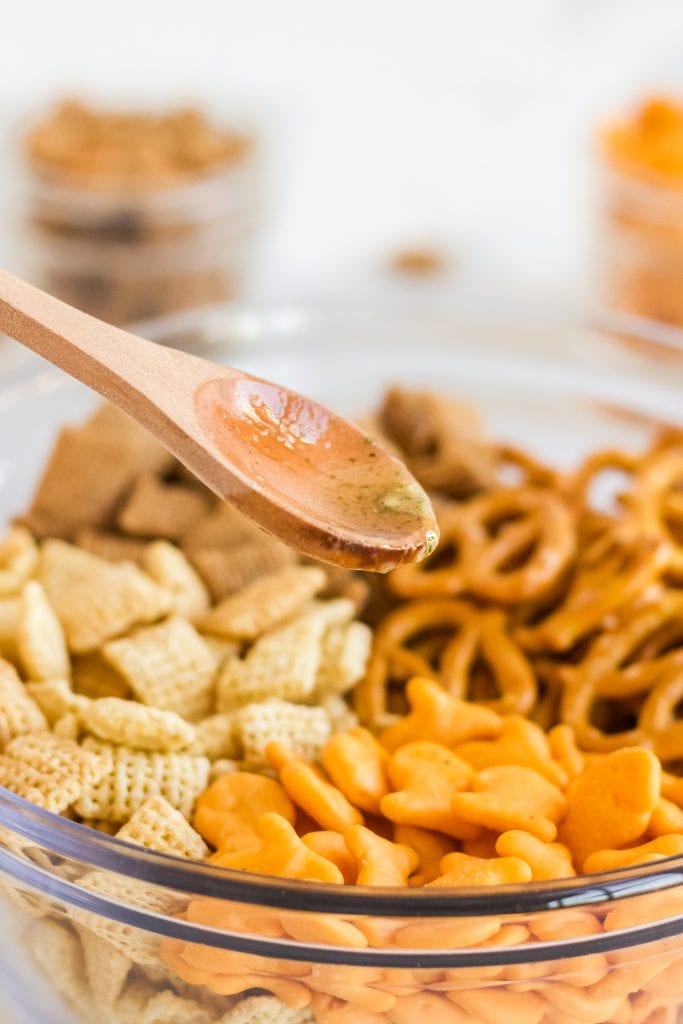 wooden spoon with sauce pouring on top of air fryer snack mix