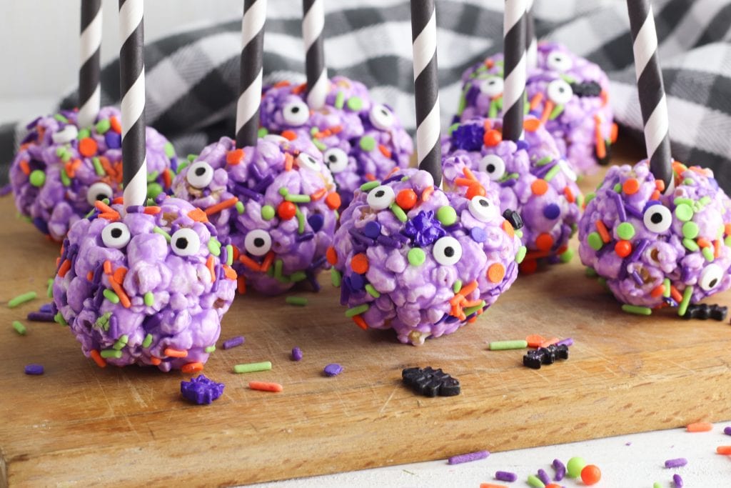 halloween popcorn balls on a wooden cutting boards with halloween sprinkles