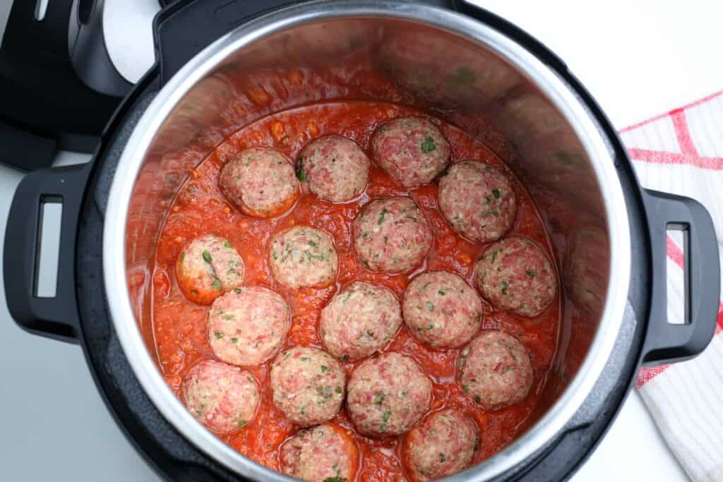 The image inside the instant pot with the sauce at the bottom, covering the trivet and the meatballs on top of the sauce. 