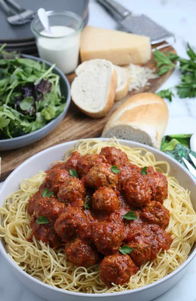 The meatballs on a bed of needles with a green salad and sliced bread in the background. 