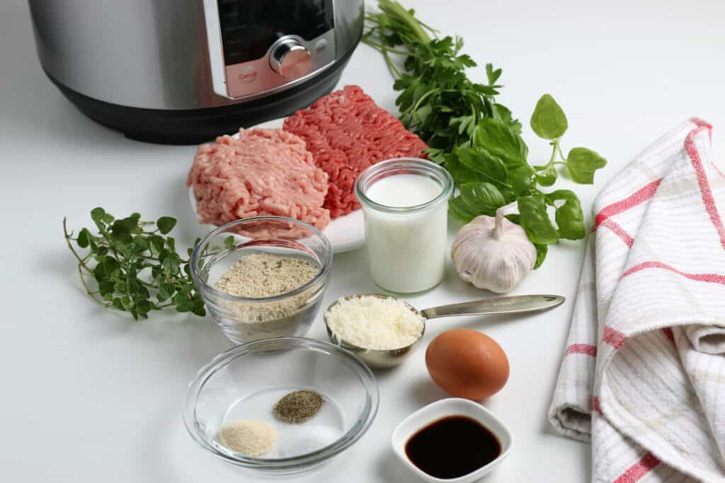 Image of all the ingredients like an egg, ground meat, and spices for this meatball recipe with an instant pot in the background. 