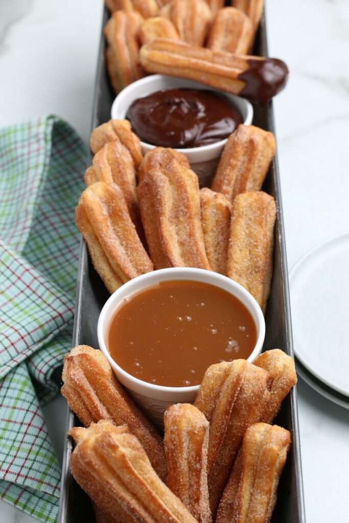 air fryer churros in a silver bin with dipping sauces