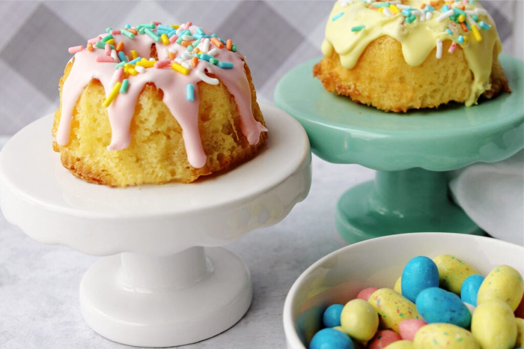 mini bundt cakes on green and white cake stands next to a bowl of candy eggs