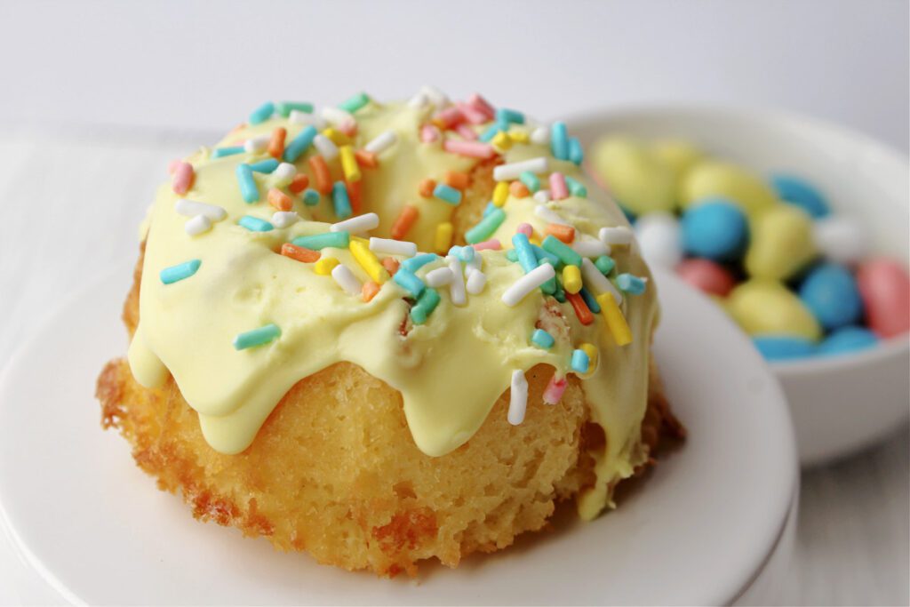 mini bundt cake with yellow icing and pastel spinkles on a white pedestal