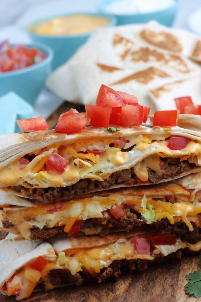 copycat crunchwrap supreme with tomato cut in hald and stacked on a cutting board