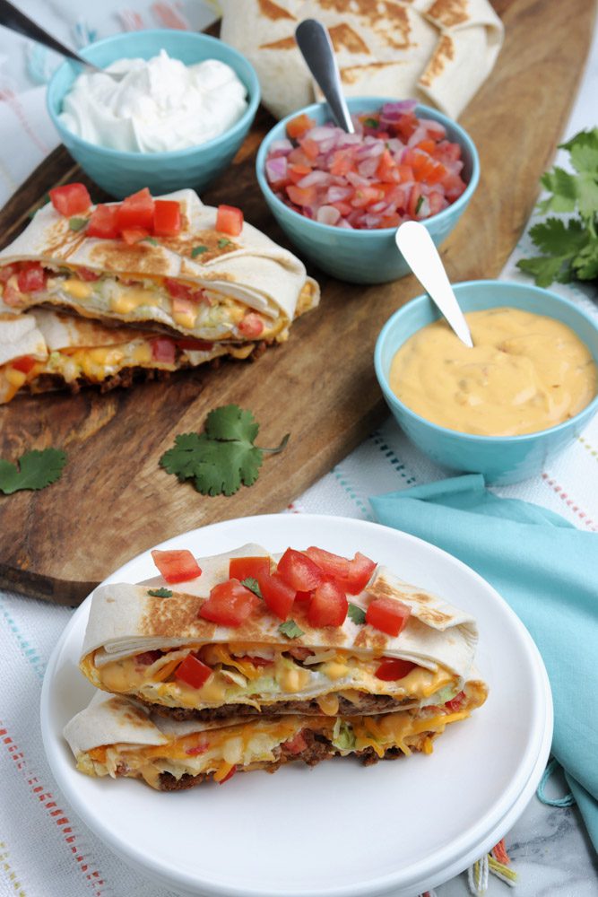copycat crunchwrap supreme on a stack of white plates with toppings on cutting board
