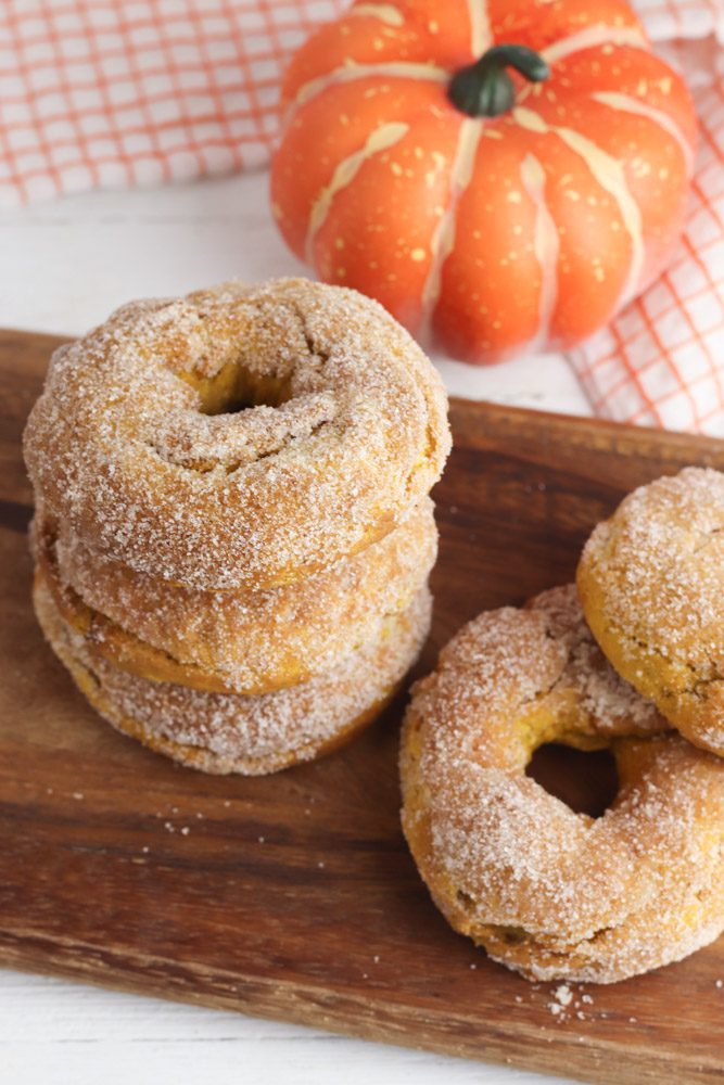 pumpkin donuts stacked on a wooden cutting board
