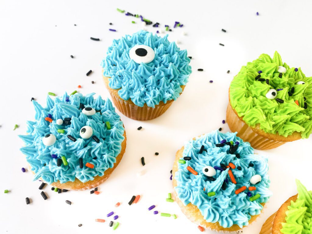 blue and green monster cupcakes on a white counter