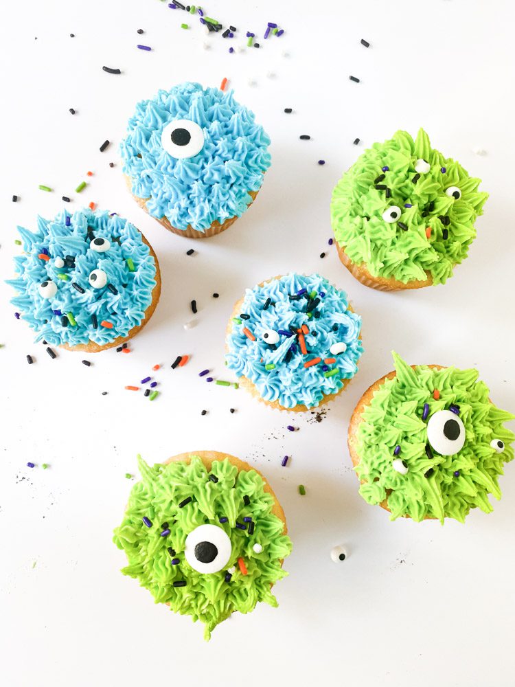 green and blue monster cupcakes sitting on halloween sprinkles