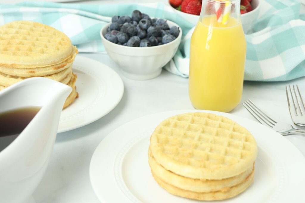 air fryer frozen waffles on white plate with orange juice and blue berries in white bowl