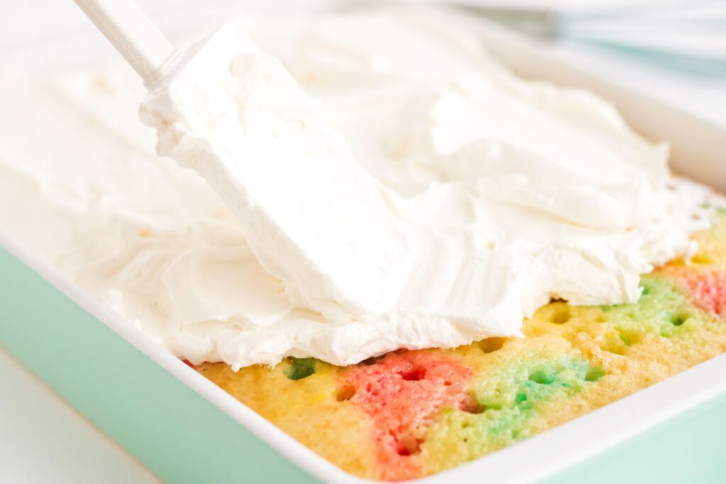 adding whipped cream to baked rainbow poke cake