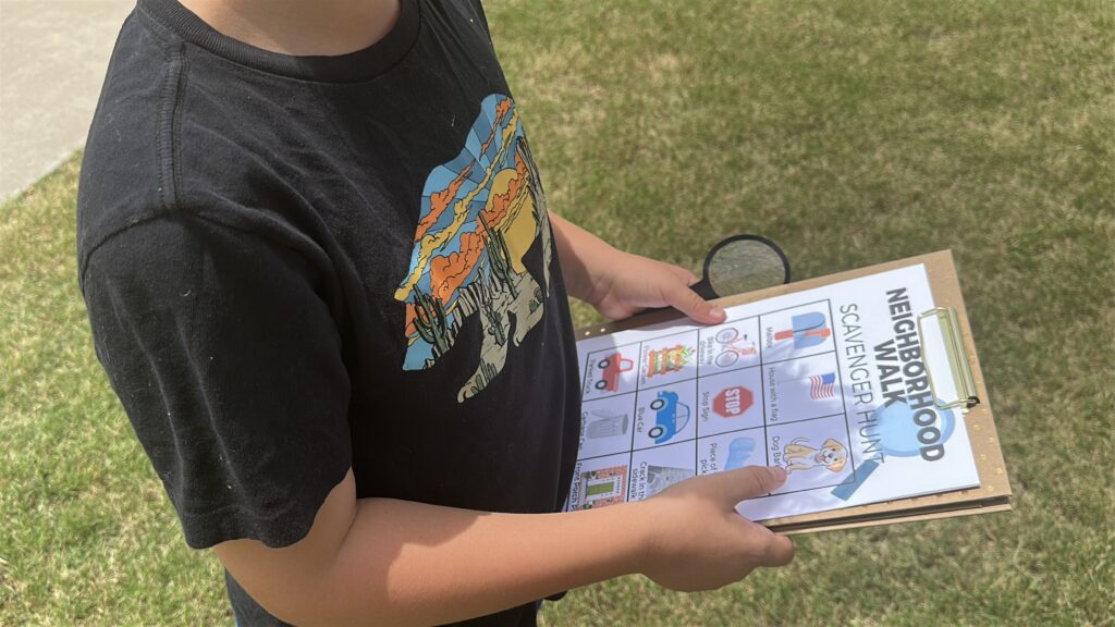 boy holding clipboard outside with neighborhood walk scavenger hunt