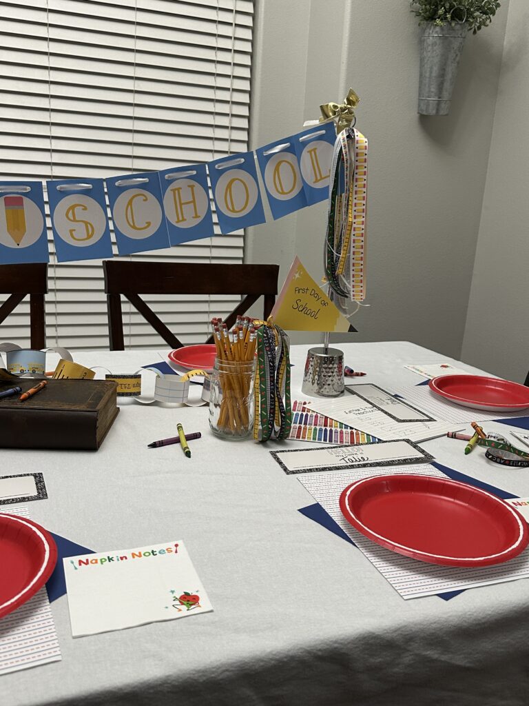 Side view of a classroom-style setup with a “BACK TO SCHOOL” banner, festive pencil-themed ribbon decorations, and jars of school supplies.