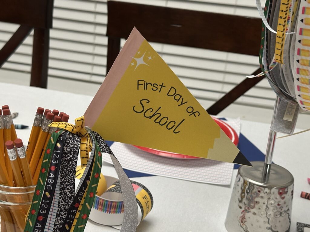 Yellow "First Day of School" flag centerpiece in a mason jar filled with pencils, decorated with measuring tape and school-themed ribbons.
