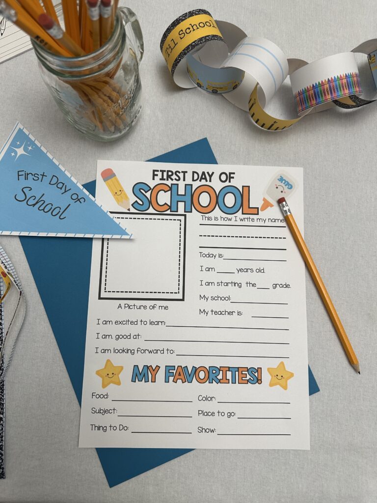 First Day of School printable laid flat on a blue folder with a pencil on top, surrounded by school supplies like ribbon wands, crayons, and a first day of school pennant.
