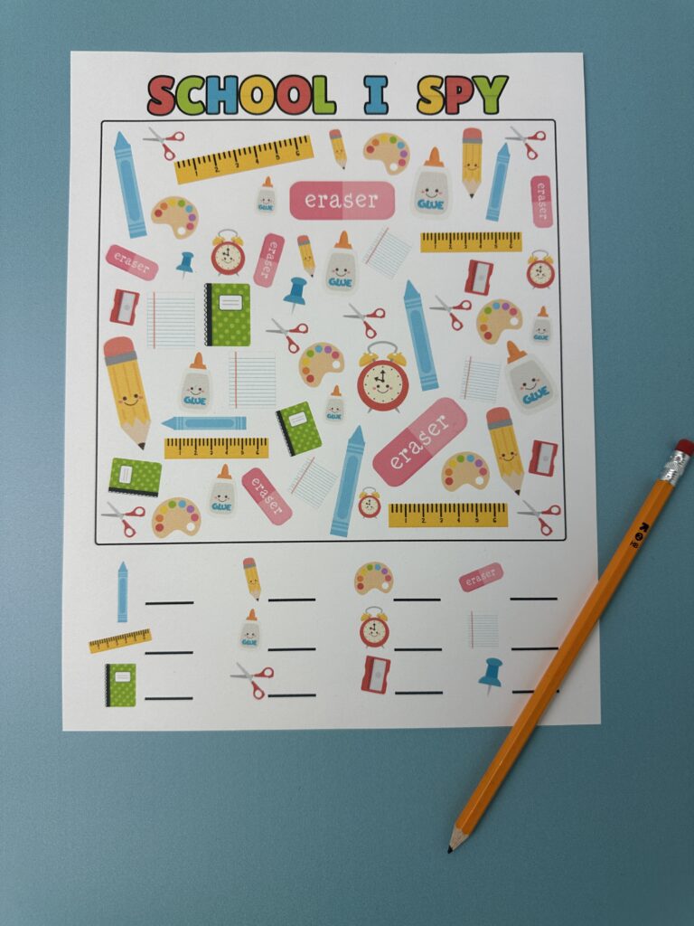 Overhead photo of the School I Spy printable placed on a blue surface with a sharpened yellow pencil to the side. The image shows the full printable with the search area and answer blanks clearly visible.