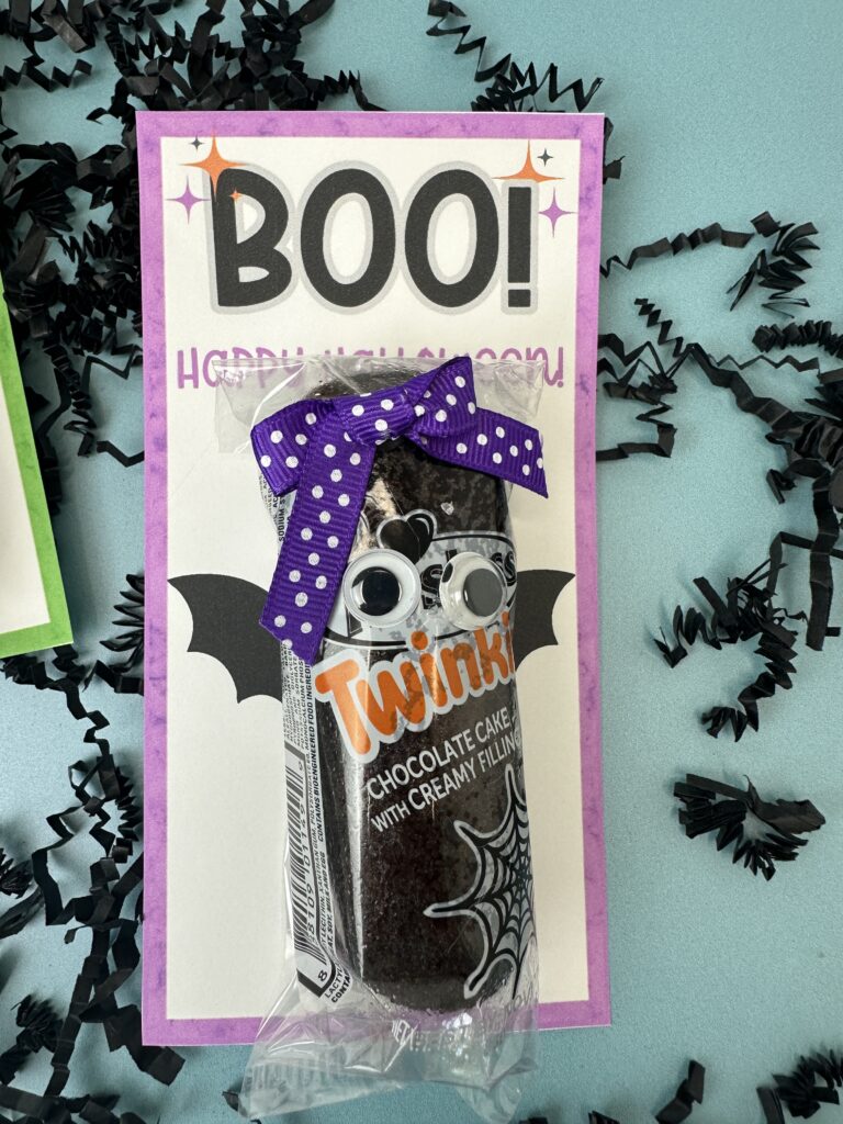 Close-up of Halloween snack cake bat with googly eyes, purple polka dot bow, and printable “BOO! Happy Halloween” tag.