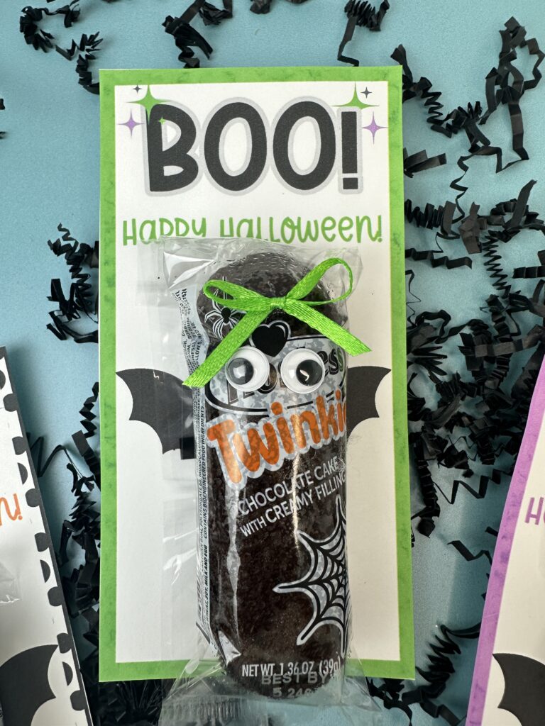 Halloween snack cake bat with green bow, googly eyes, and printable “BOO! Happy Halloween” tag on green border.