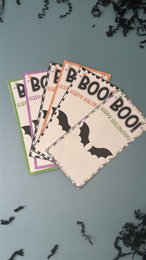 Close-up sheet of Halloween bat treat printables with “BOO! Happy Halloween” text and bat wings in orange and multicolor borders.