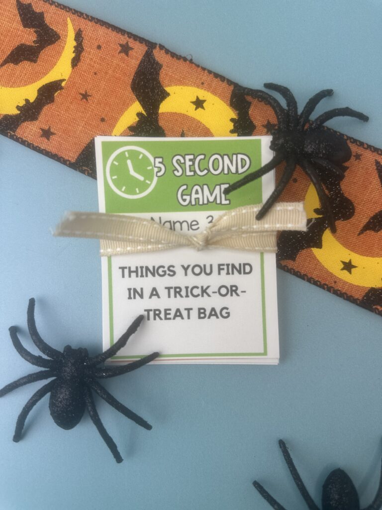 Stack of Halloween 5 Second Game cards tied with a cream ribbon, with text “Things you find in a trick-or-treat bag,” styled with spiders and Halloween ribbon.