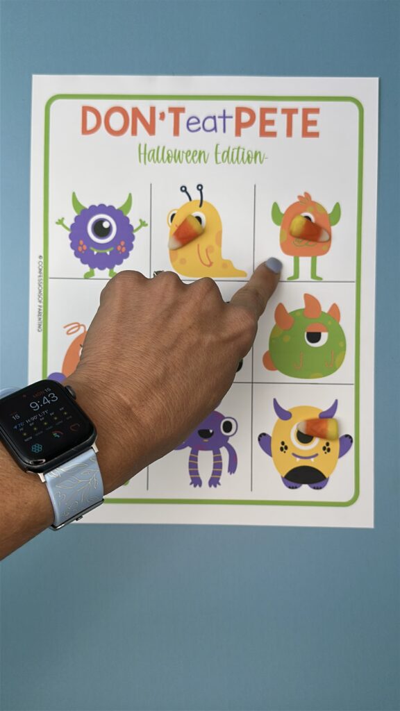A finger pointing to one of the monsters on the "Don't Eat Pete – Halloween Edition" game board. Several candy corn pieces are placed on top of different monster characters.