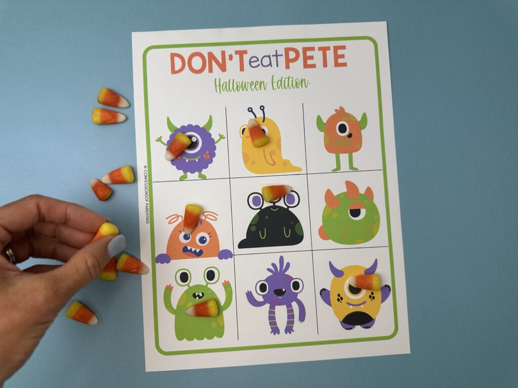 A hand placing candy corn on a monster illustration while several other squares on the "Don't Eat Pete – Halloween Edition" game board already have candy corn on them.