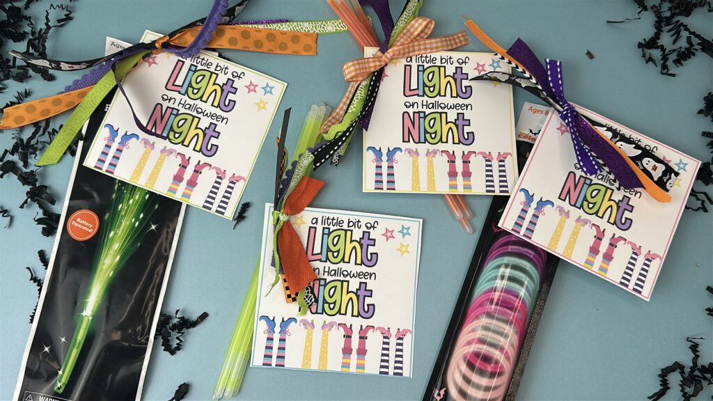 Multiple Halloween light stickss tied to glow sticks with ribbons in various colors with a tag on it that says a little bit of light on halloween night. 