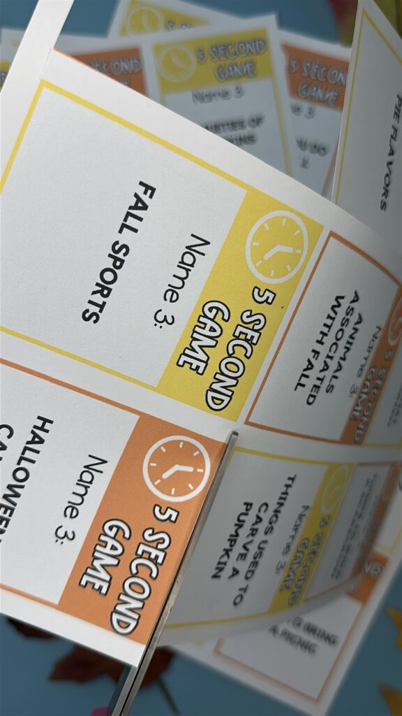 Close-up of printed 5 Second Game cards with prompts including “Fall sports” and “Things used to carve a pumpkin.” getting cut