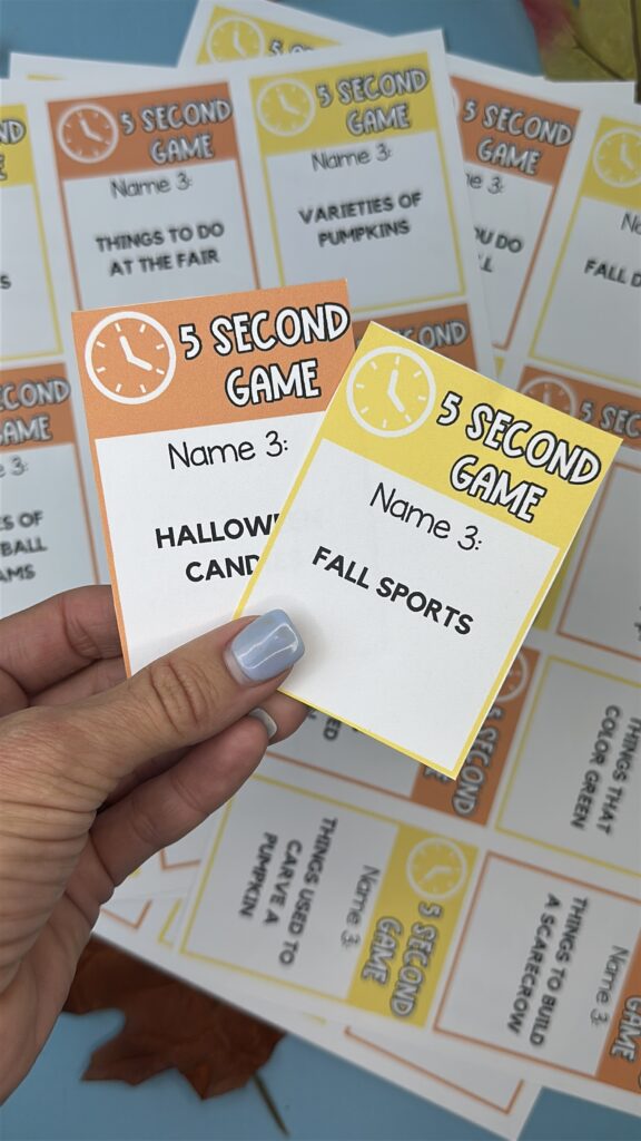 Hand holding two fall 5 Second Game cards labeled “Halloween candies” and “Fall sports” above a colorful spread of game cards.