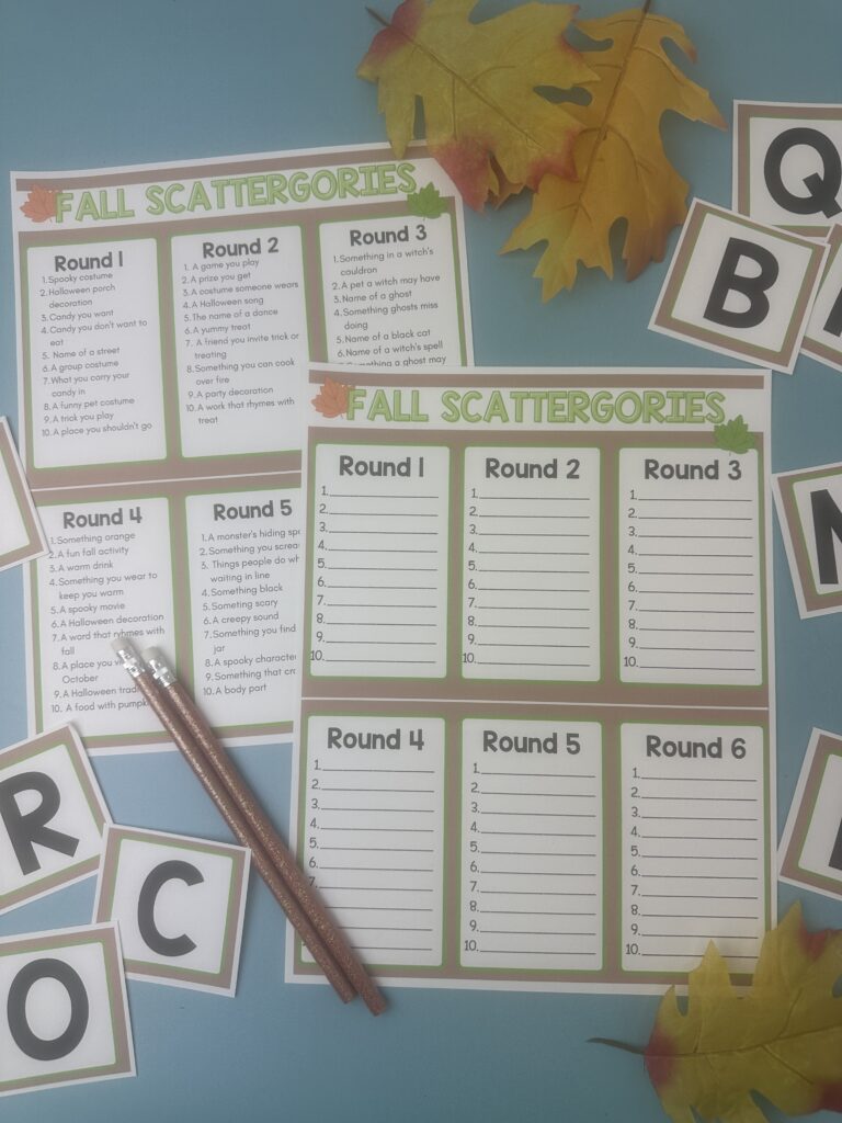 Printable Fall Scattergories game setup with blank answer sheets and themed prompts, placed with letter cards, autumn leaves, and pencils on a blue background.