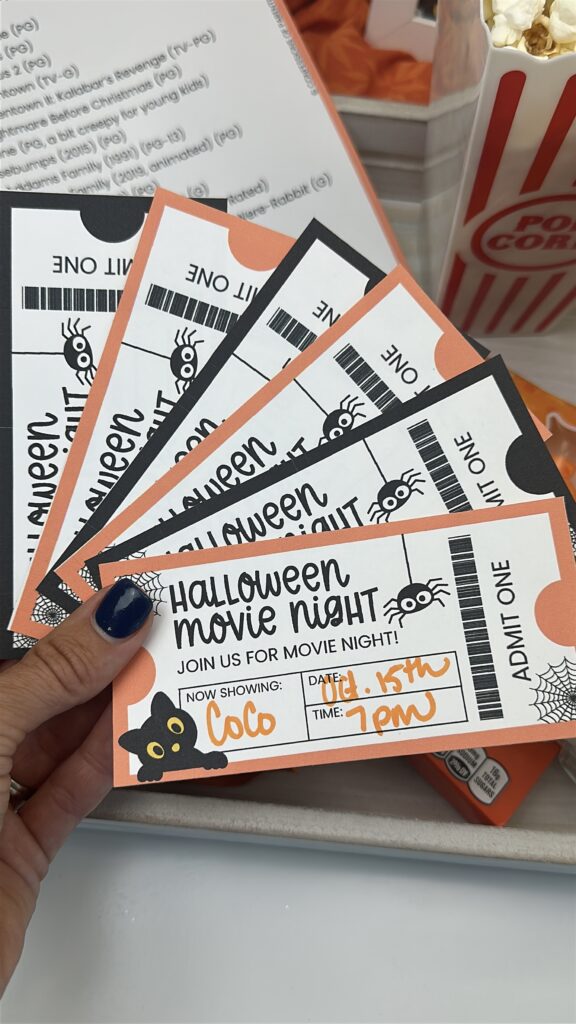 Hand holding Halloween movie night tickets with popcorn and candy in the background.