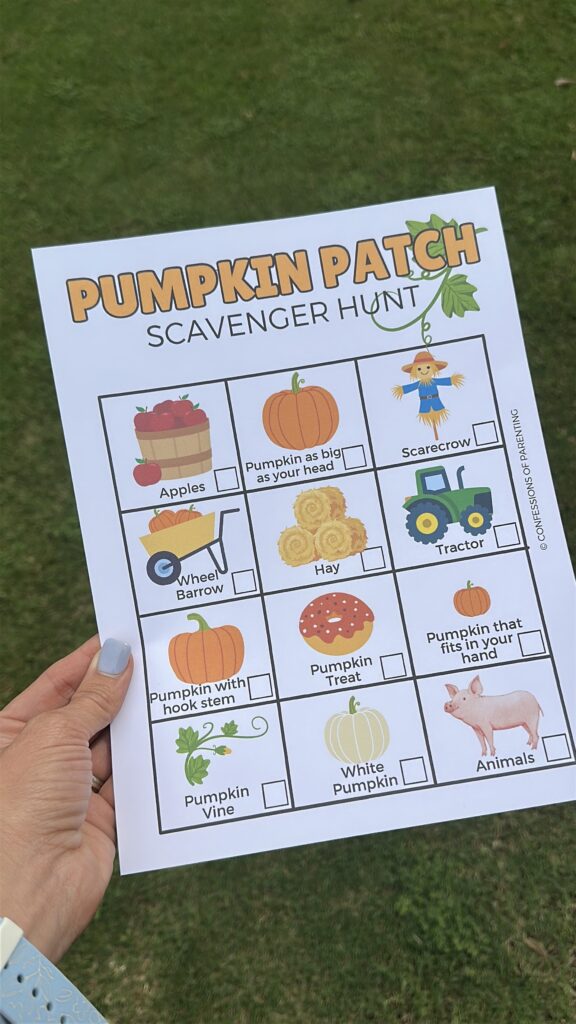 A hand holding the Pumpkin Patch Scavenger Hunt printable outside on the grass, ready for the activity.