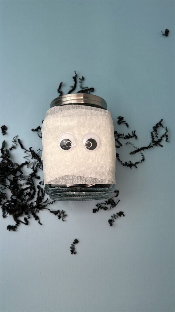 Halloween mummy jar wrapped in crepe paper with large googly eyes attached.