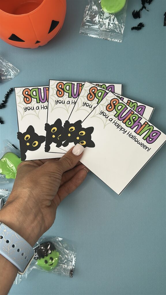 Hand holding four printable Halloween tags that read “Squishing You a Happy Halloween” with squishy toys.
