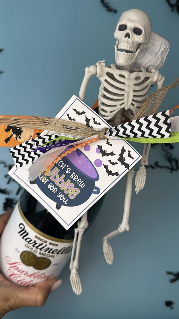A bottle of Martinelli’s sparkling cider decorated for Halloween with a skeleton figurine, colorful ribbon, and a tag that reads "Witch’s Brew Bubbles Just for You."