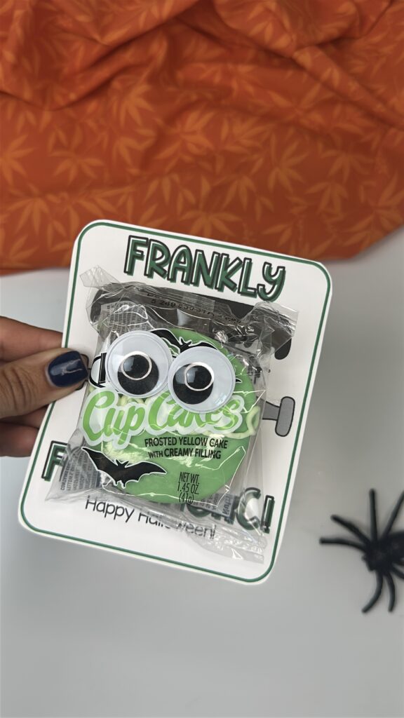 Hand holding a Hostess cupcake with googly eyes attached to a “Frankly You’re Fang-tastic” Halloween tag.