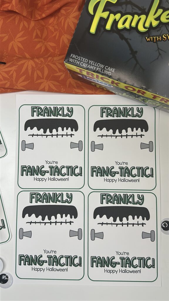 Halloween “Frankly You’re Fang-tastic” setup with tags, green cupcakes, and spiders on an orange fabric background.