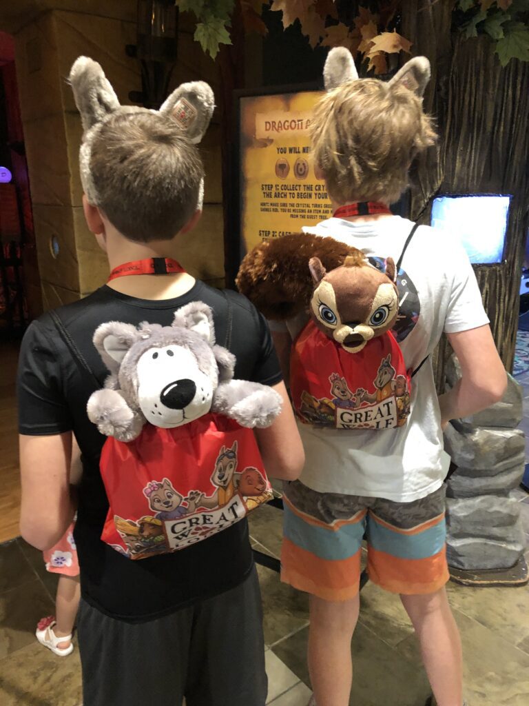 Two boys with wolf ears and stuffed animals in red Great Wolf Lodge drawstring bags ready for MagiQuest adventure at Great Wolf Lodge Grapevine TX.
